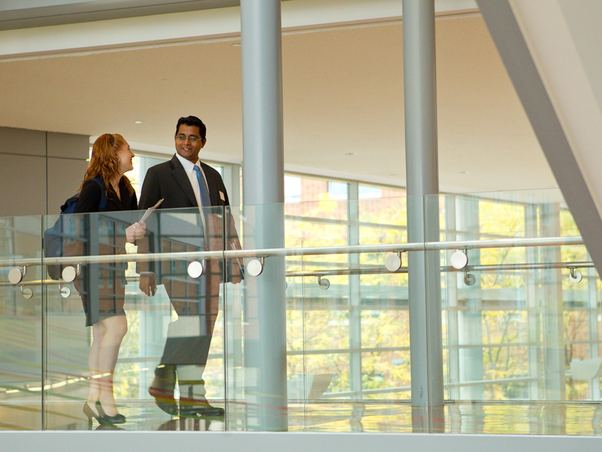 Two students, one male, one female, walk across the second-floor bridge in the Business Building Atrium.