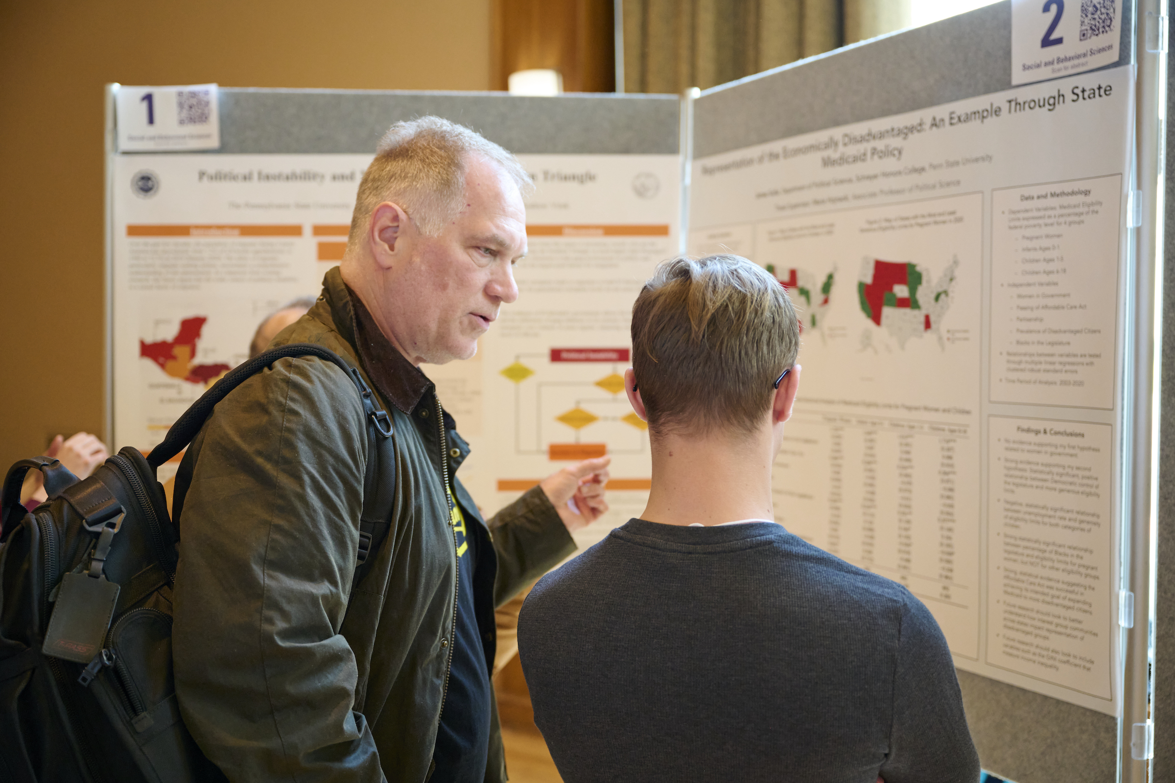 Faculty judge talking with student in front of research poster