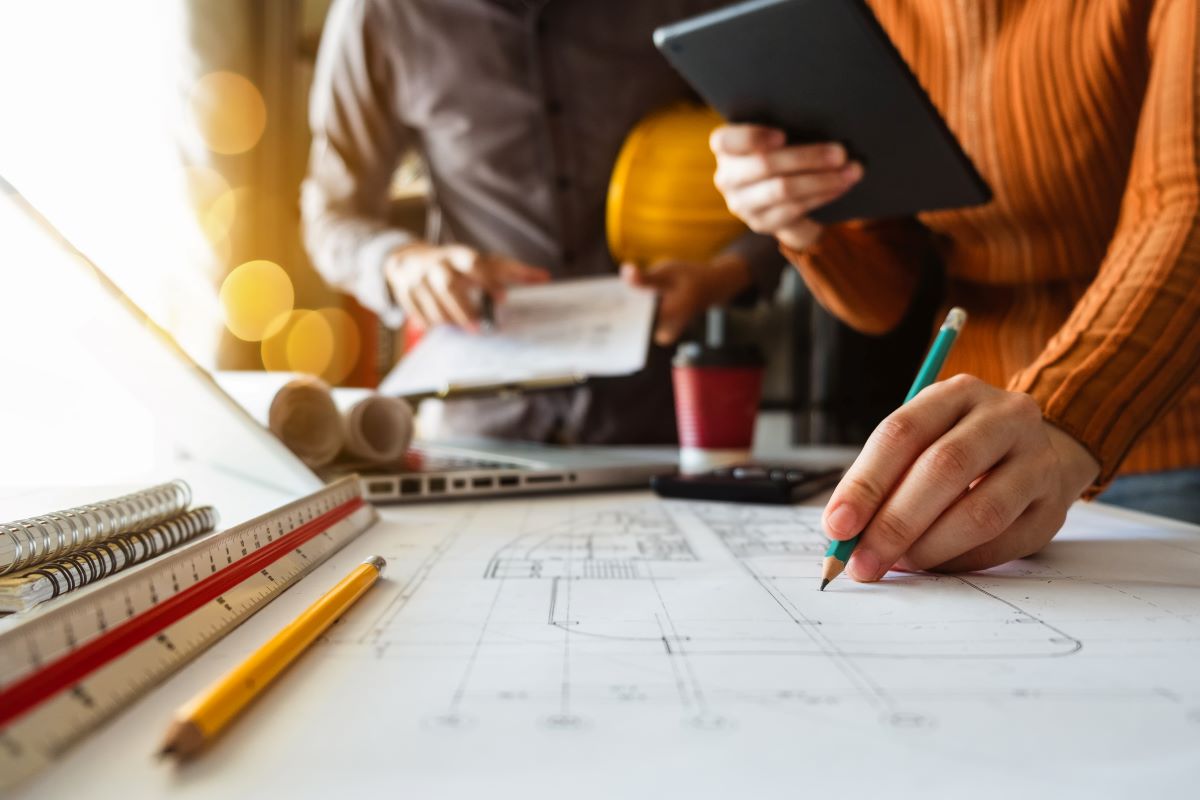 Two colleagues discussing data working and tablet, laptop with on on architectural project at construction site at desk in office