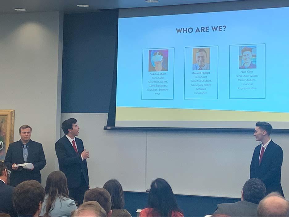 Three students with a PowerPoint presentation projected behind them.