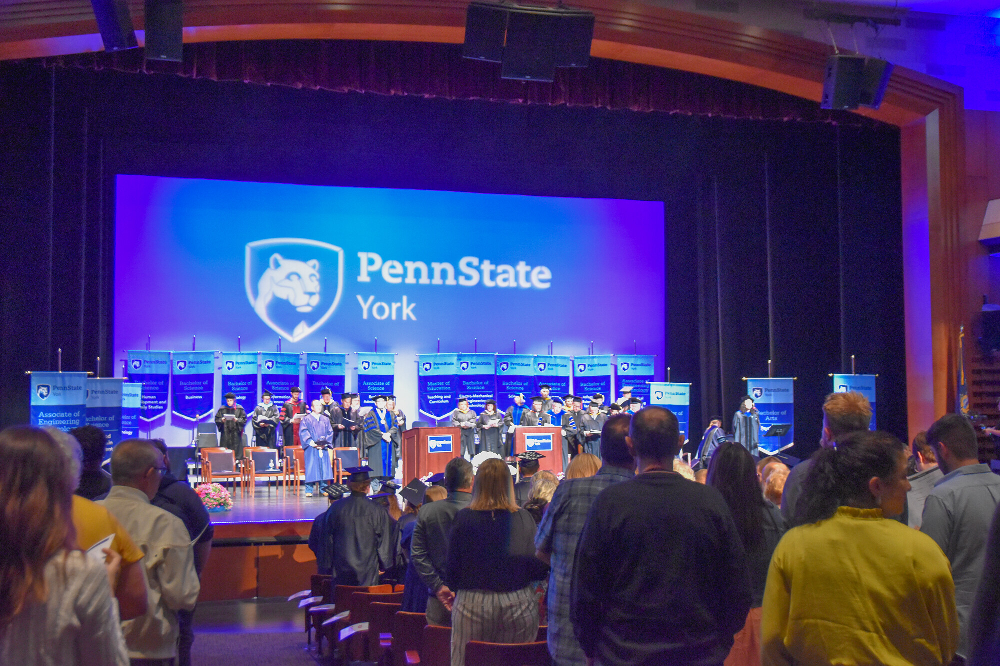 Theatre filled with people watch a commencement ceremony on stage