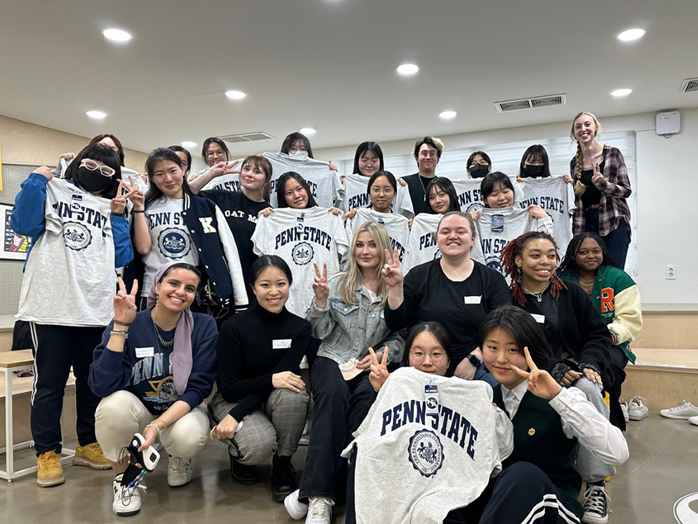 Penn State KOR 499 students interacting with female Korean high schoolers and exchanging Penn State shirts as gifts.