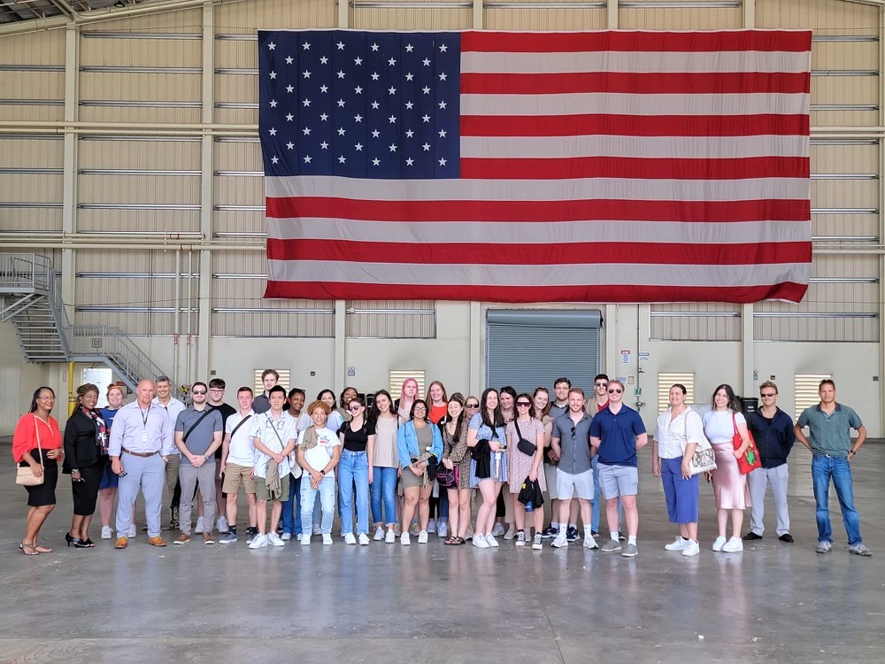 Students in CRIM 425 pose for a group picture below a large American flag at the Drug Enforcement Administration in Curaçao