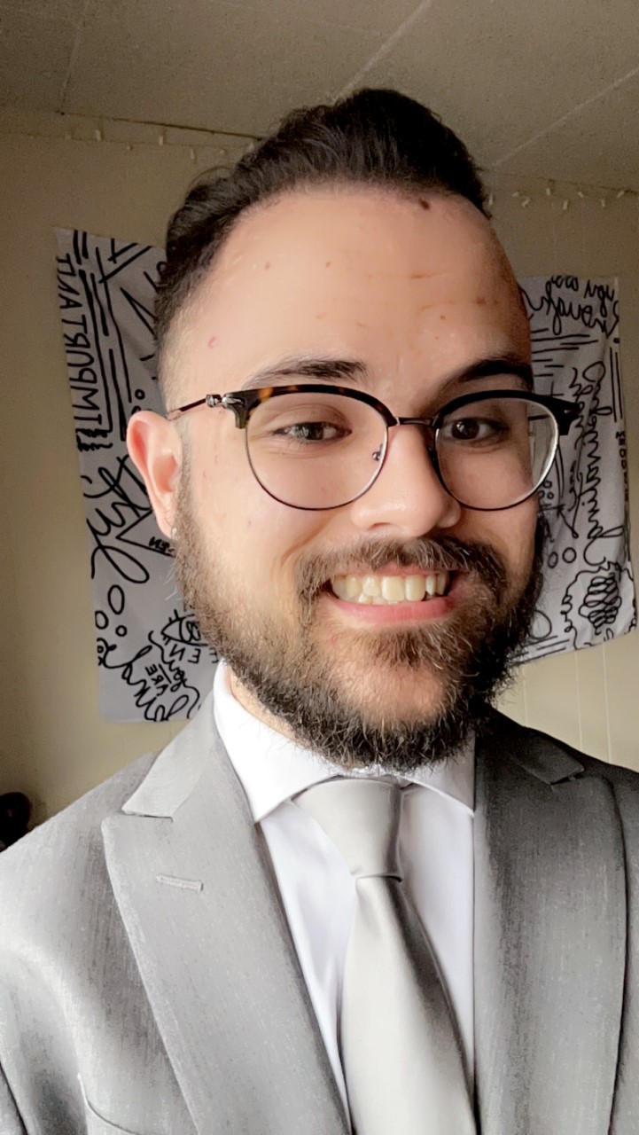 Head shot of a young man with dark hair and dark-rimmed glasses smiling