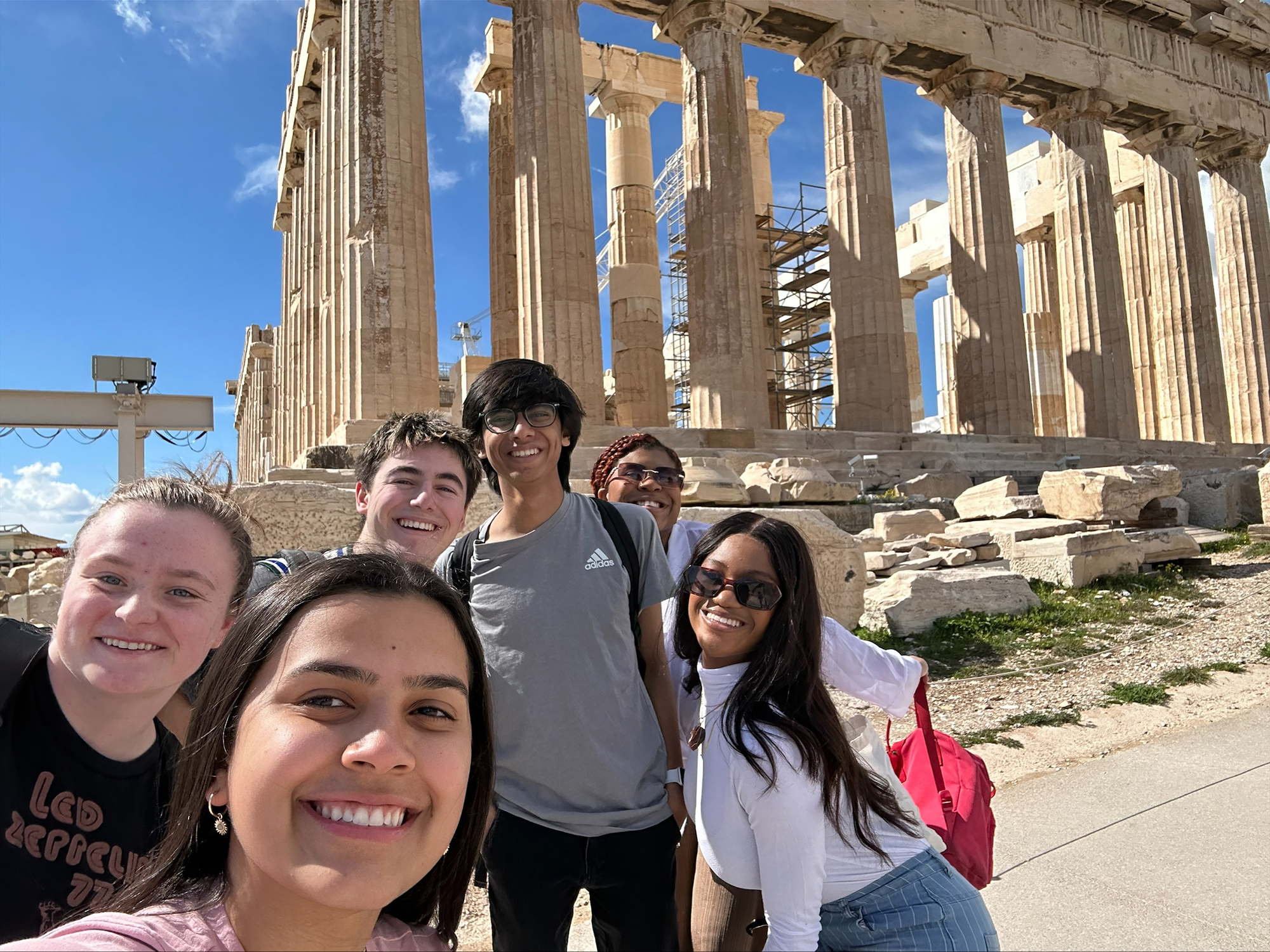 Group photo with Michelle Kengkart (center) and, left to right, Grace Pilch, Owen Perry, Mihir Kulkarni, Leila Filien and De'jah Coates, posing in front of the Parthenon in Athens, Greece.