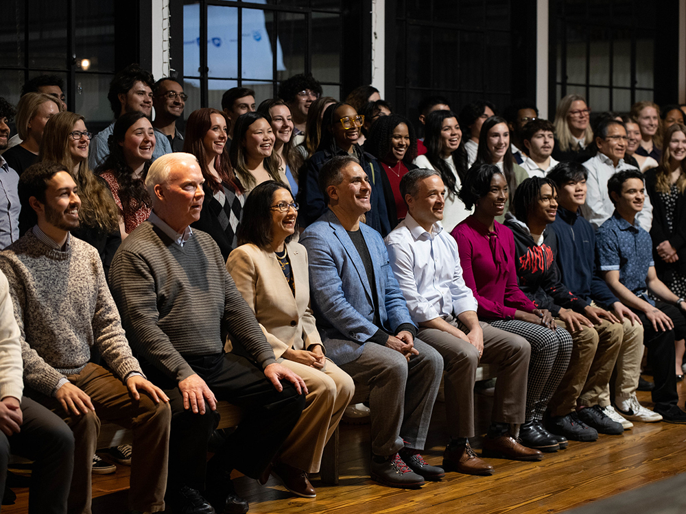 An audience consisting of three rows of people smile and look ahead 