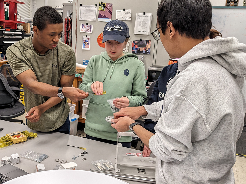 Two students pass a screwdriver to two other students who are working on a small piece of equipment. 