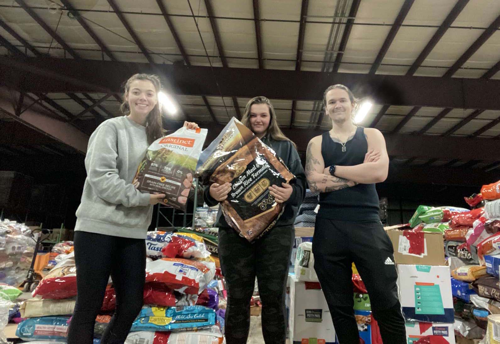 Three students standing in front of stacks of pet food in a warehouse.