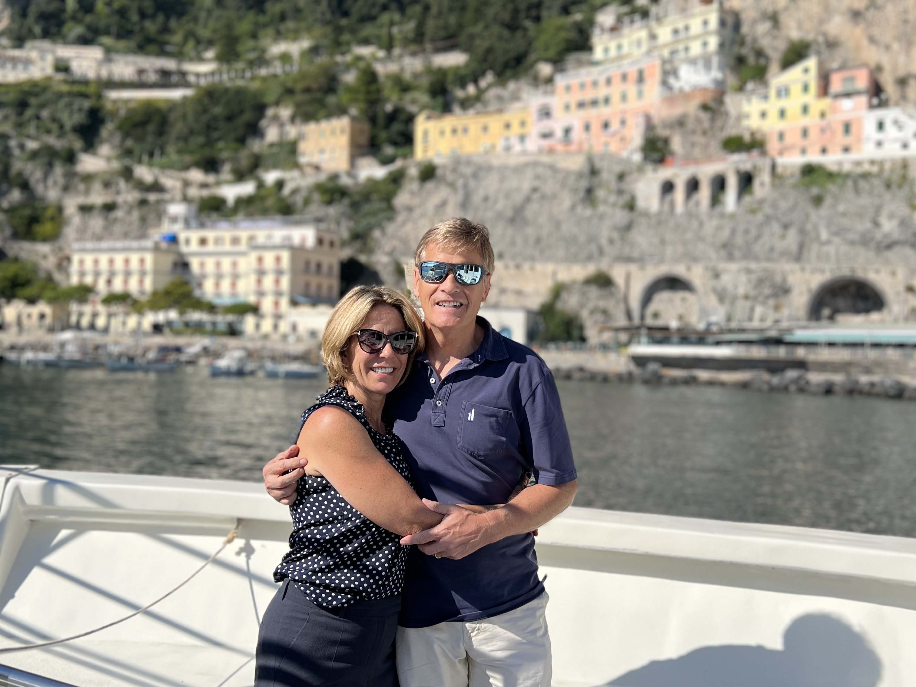 A woman and a man on a boat with the coastline behind them