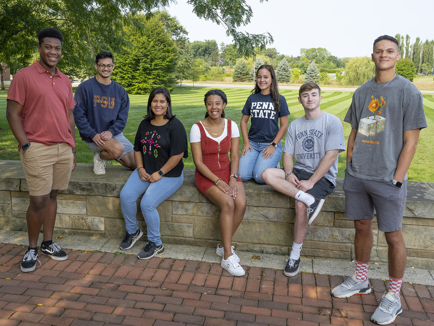 A photo of male and female Smeal students sitting and standing on the wall overlooking the meadow outside of the Business Building