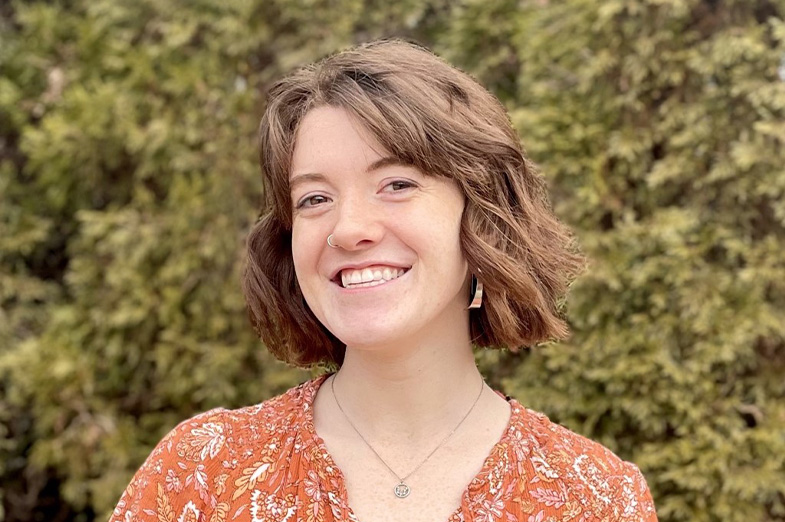 Head shot of a young woman with short brown hair posing in front of hedges