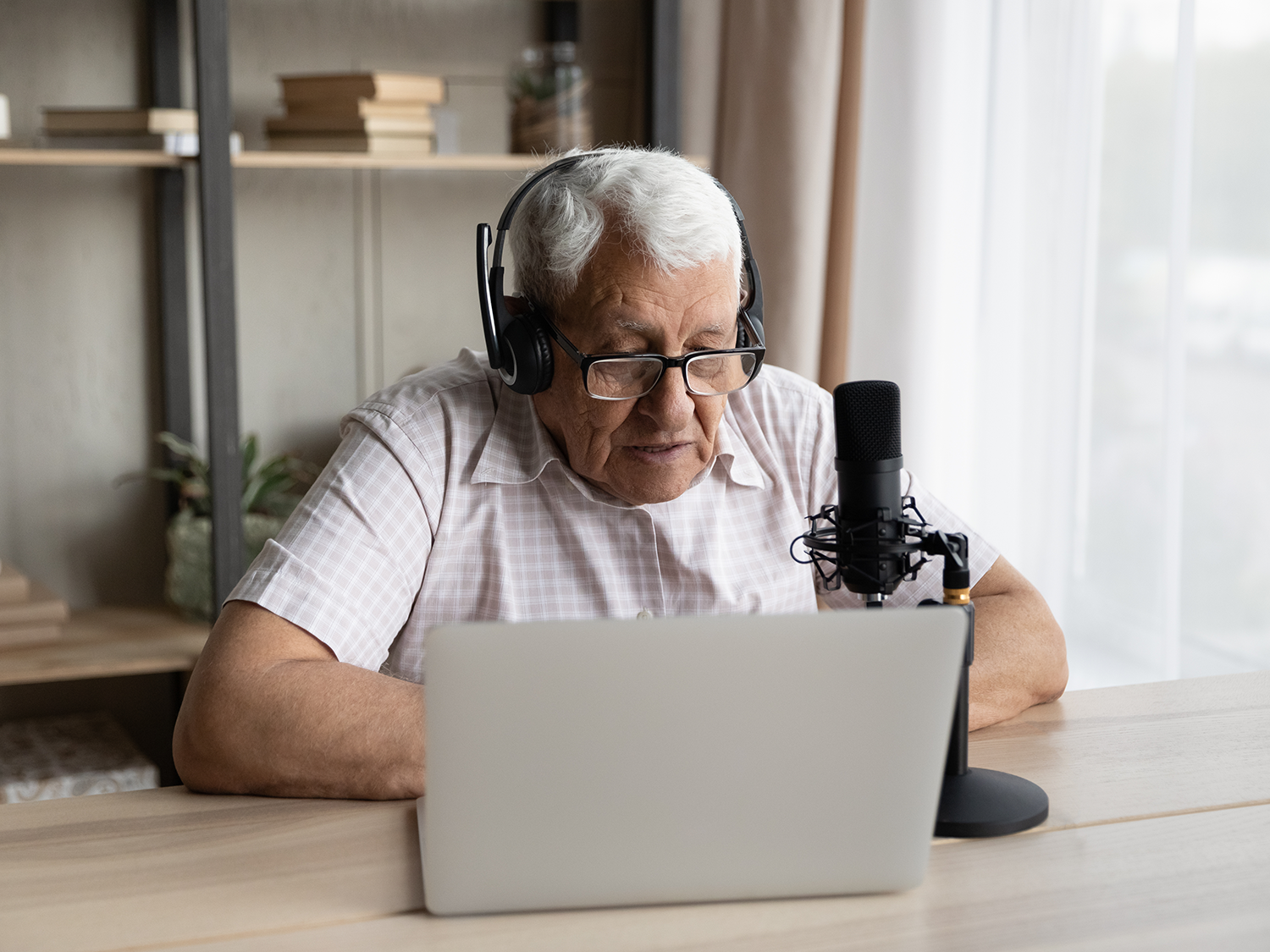 An older man sitting in front of a laptop wearing a headset and speaking into a microphone.