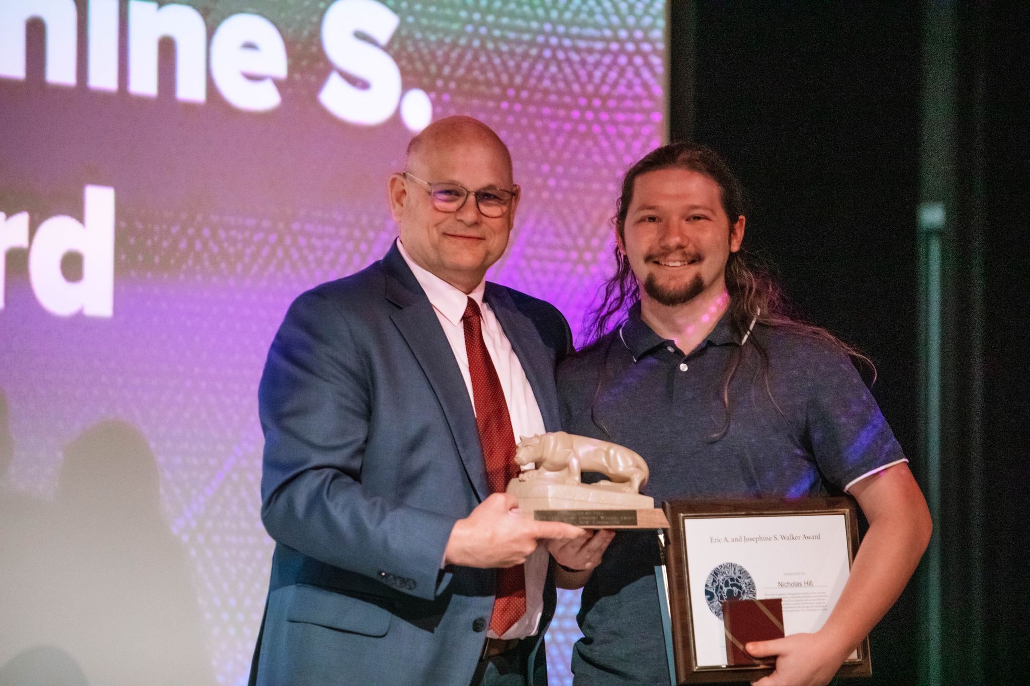 Two people stand holding a trophy