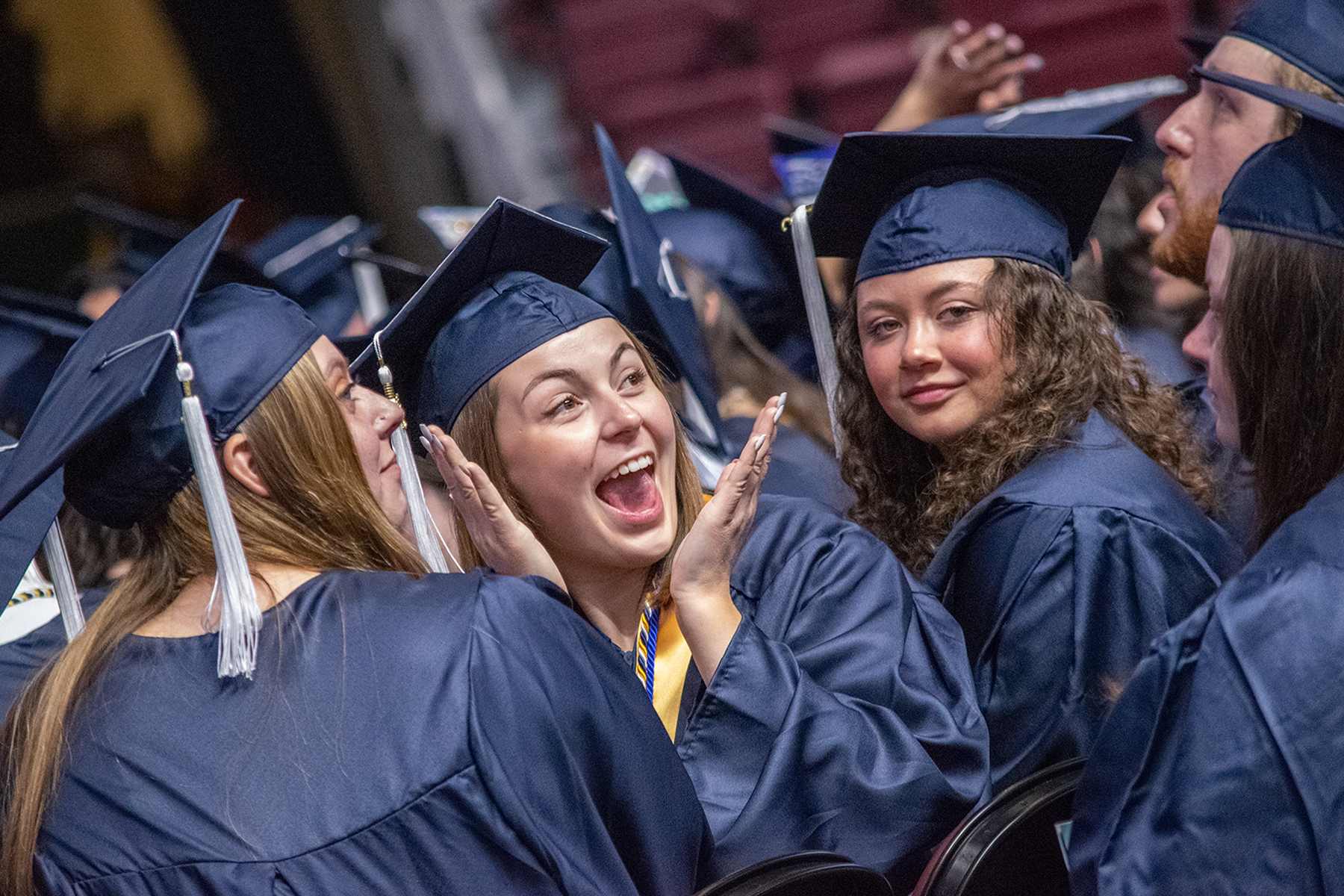 Three women students smiling in caps and gowns at commencement