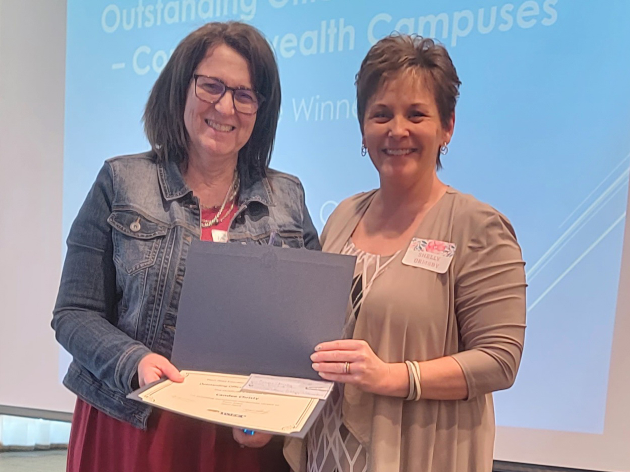 Two people standing and smiling as they hold up a portfolio containing an award