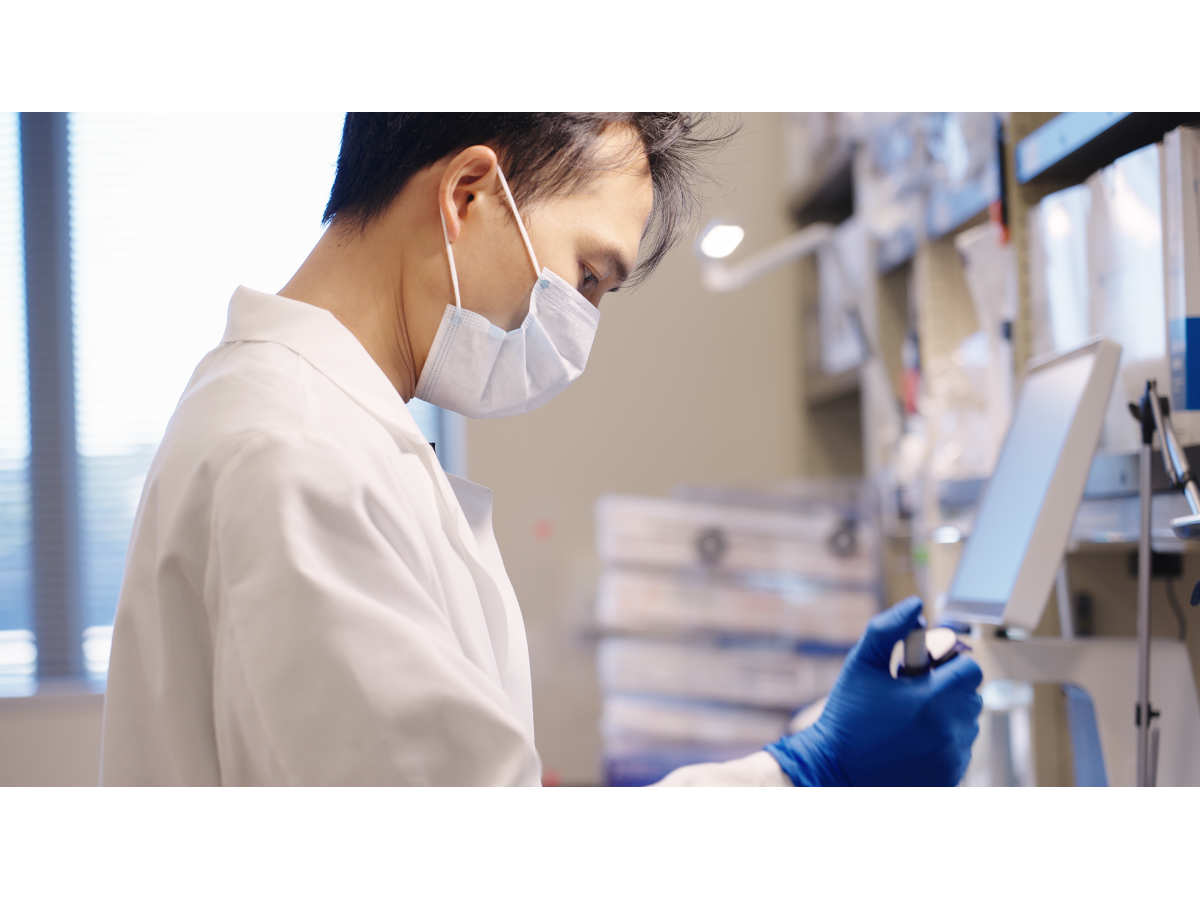 Jiaxing Chen, a bioinformatics and genomics doctoral student at Penn State College of Medicine and Penn State Huck Institutes of the Life Sciences, pipettes a solution in a laboratory while wearing gloves, a lab coat and a mask. 