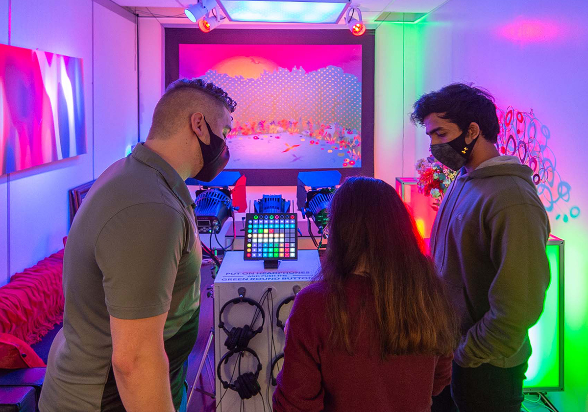 Three individuals look at a lighting board in a colorfully-lit room.