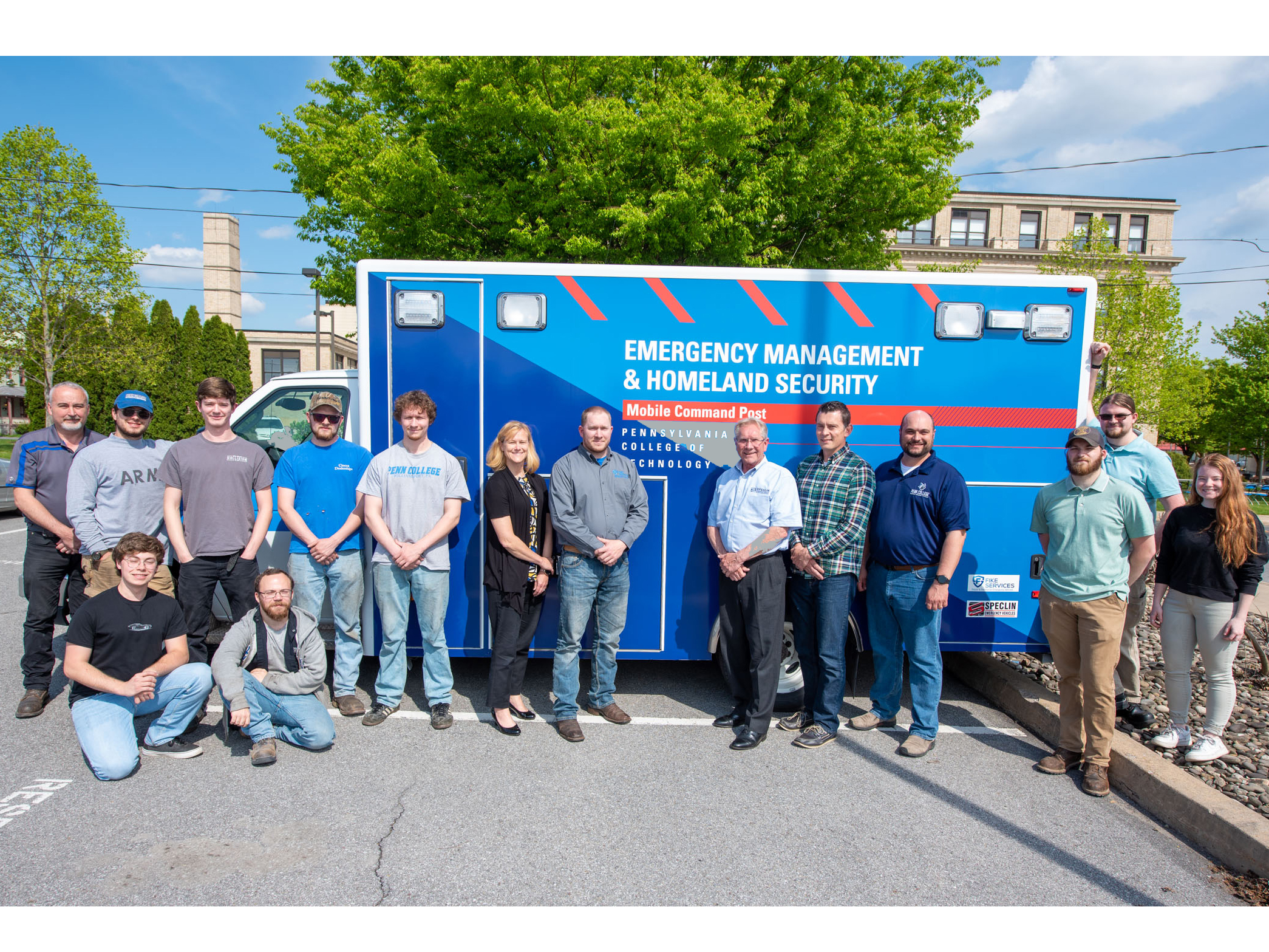 A group of people pose in front of a mobile command post vehicle