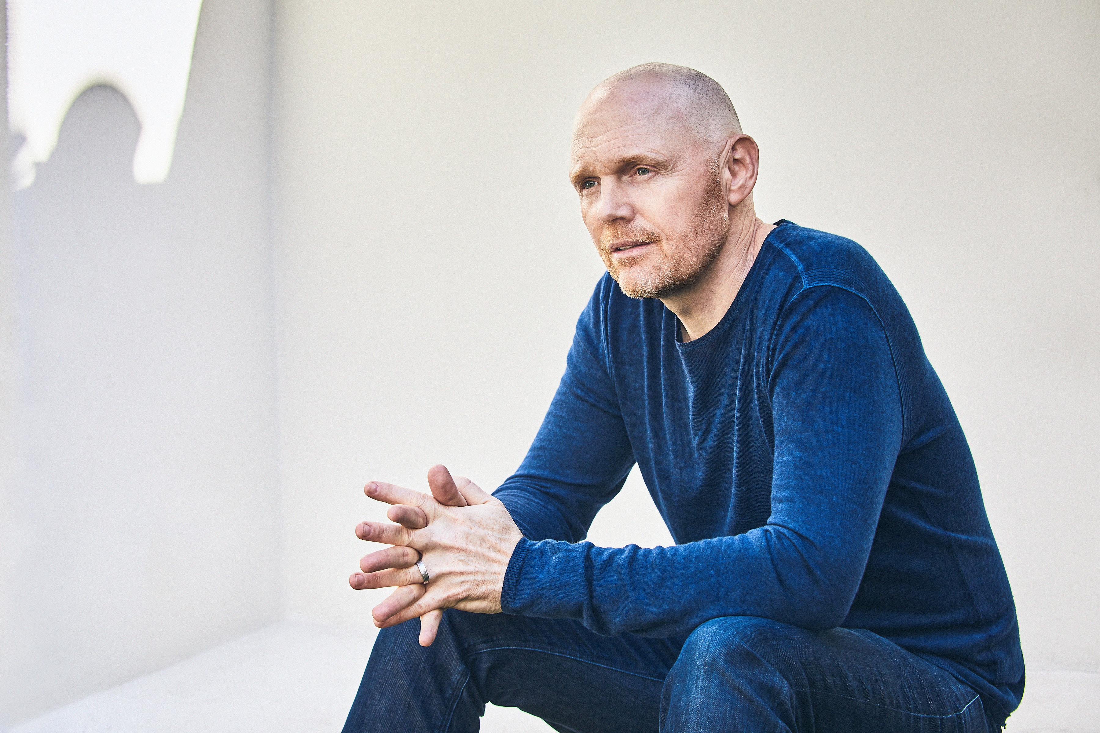 Photo of Bill Burr wearing blue jeans and a blue shirt on a white background