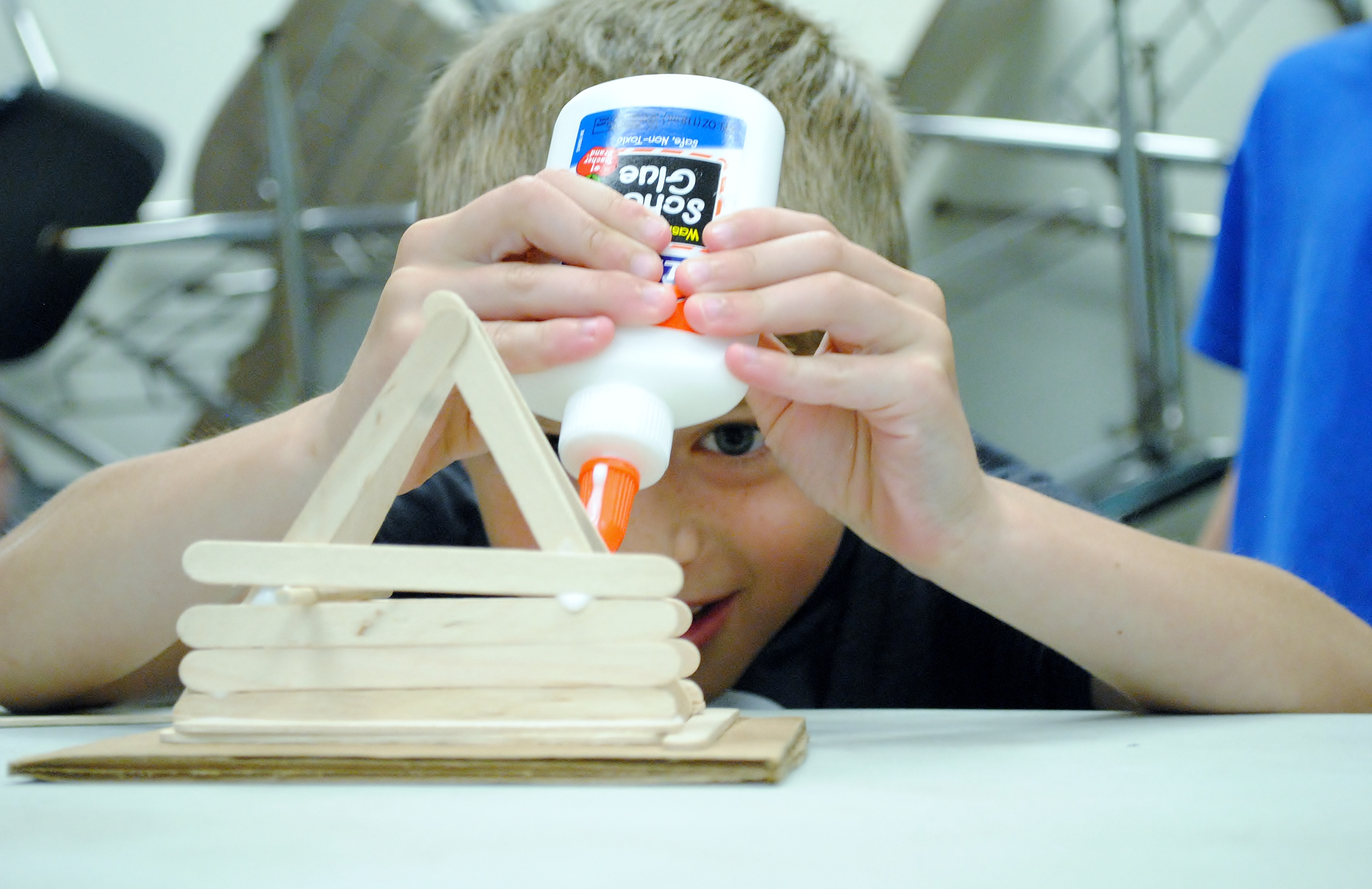 A boy builds a structure with glue and popsicle sticks.