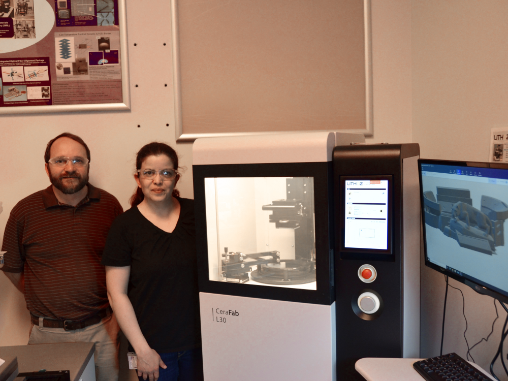 Two people standing next to a 3D ceramic printer in a lab