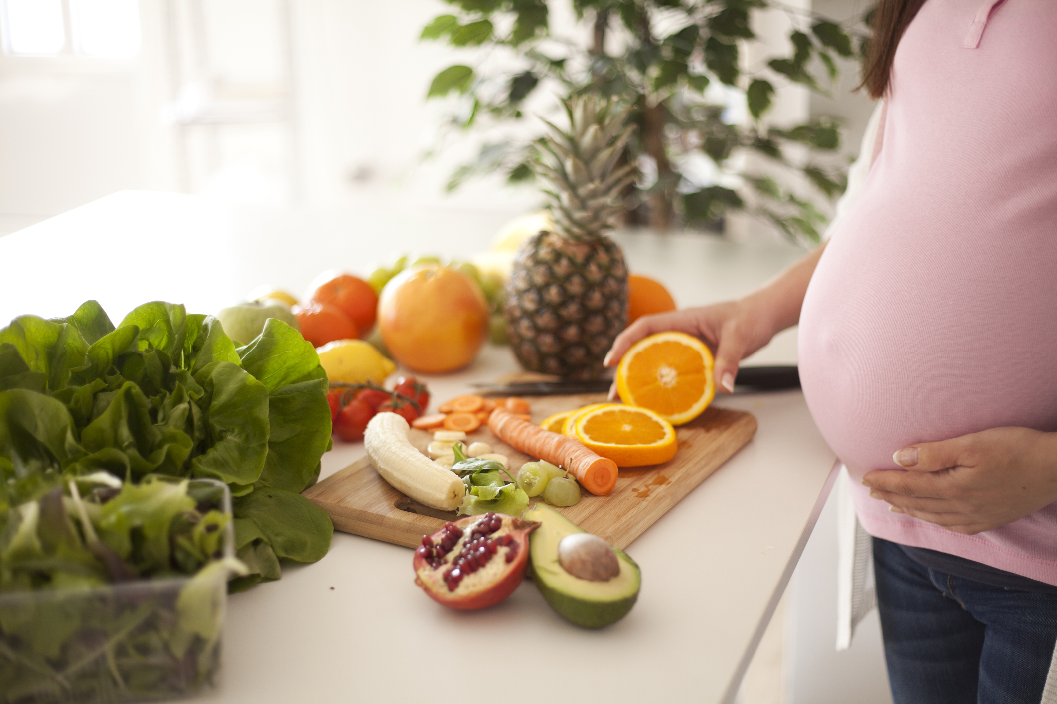 Torso of a pregnant woman in front of counter with an array of fresh fruits and vegetables