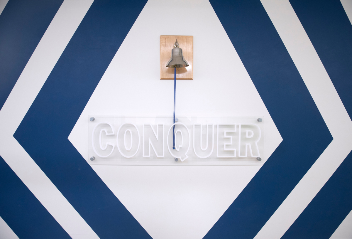 Photo shows a bell that pediatric cancer patients ring during their final cancer treatments at Penn State Health Children’s Hospital. The bell is places above a sign that says, “Conquer.”