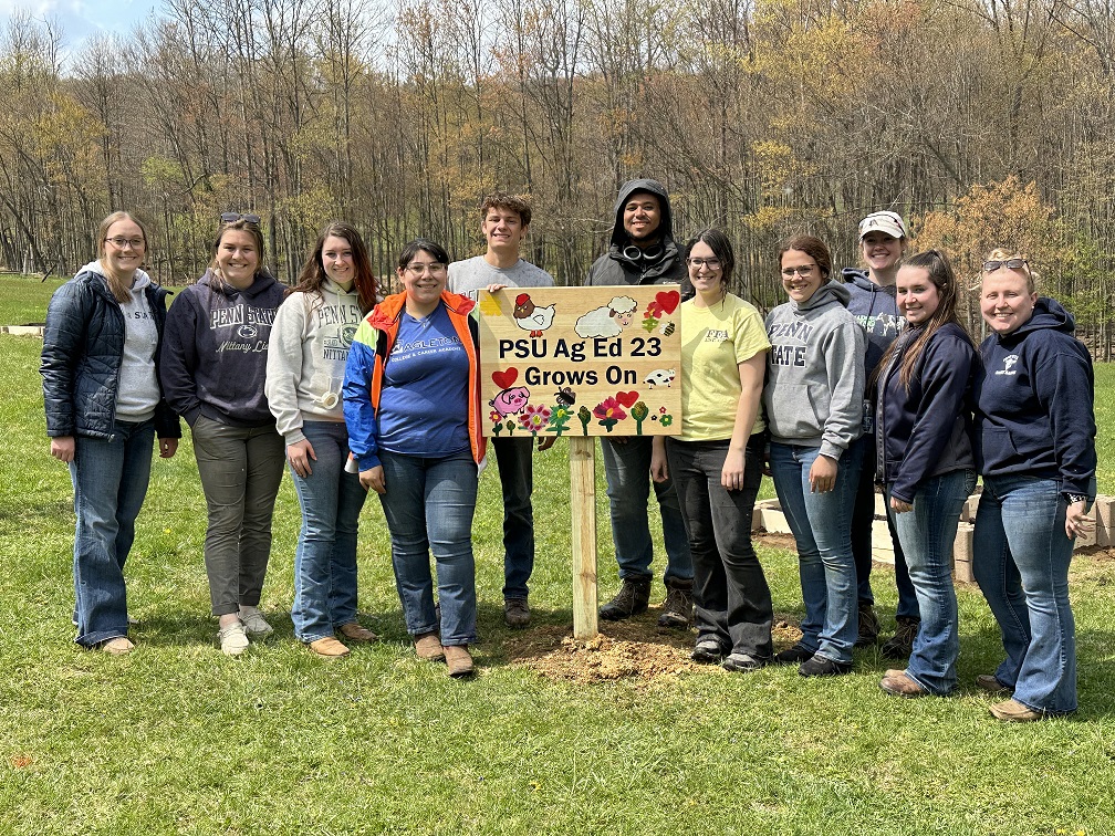 students standing around a sign, woods visible in the background