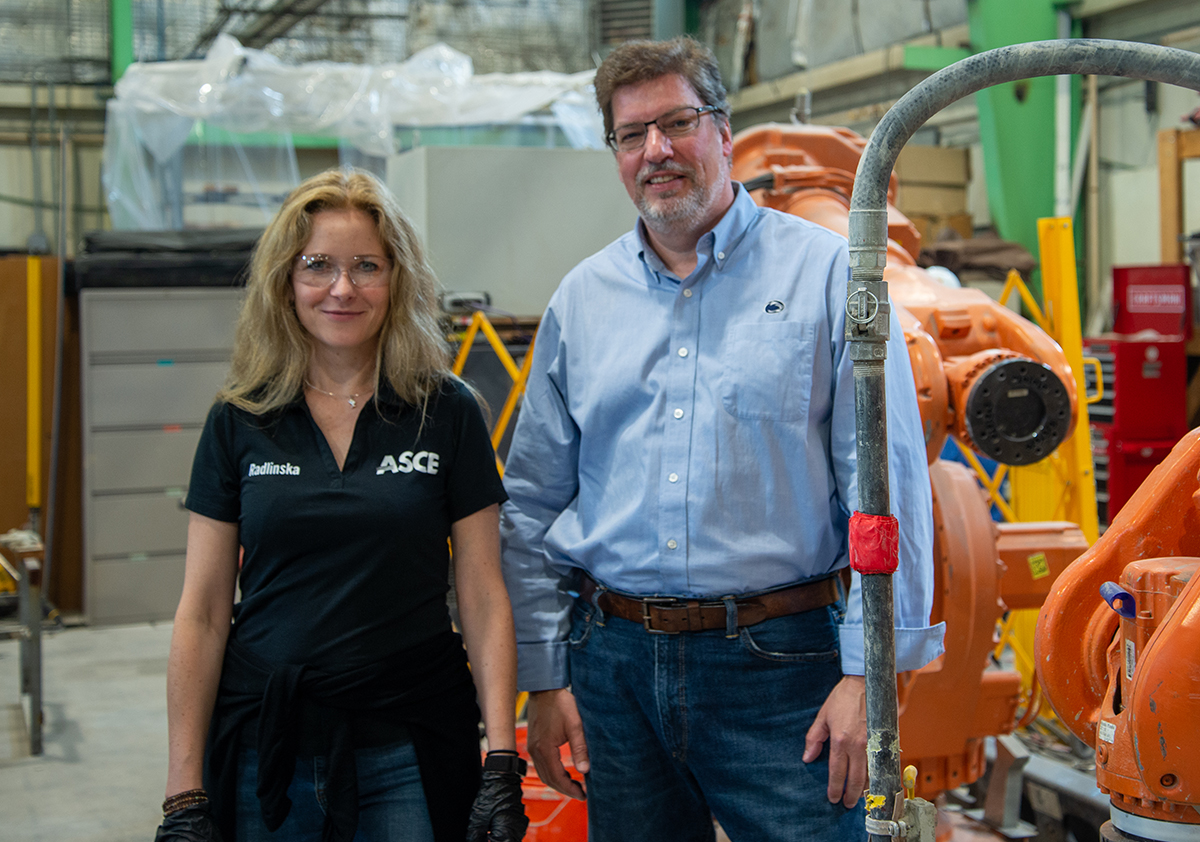 Two individuals pose in a large open lab surrounded by lab equipment.