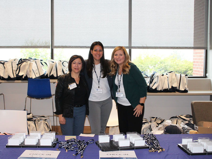 three women stand at check-in table at conference