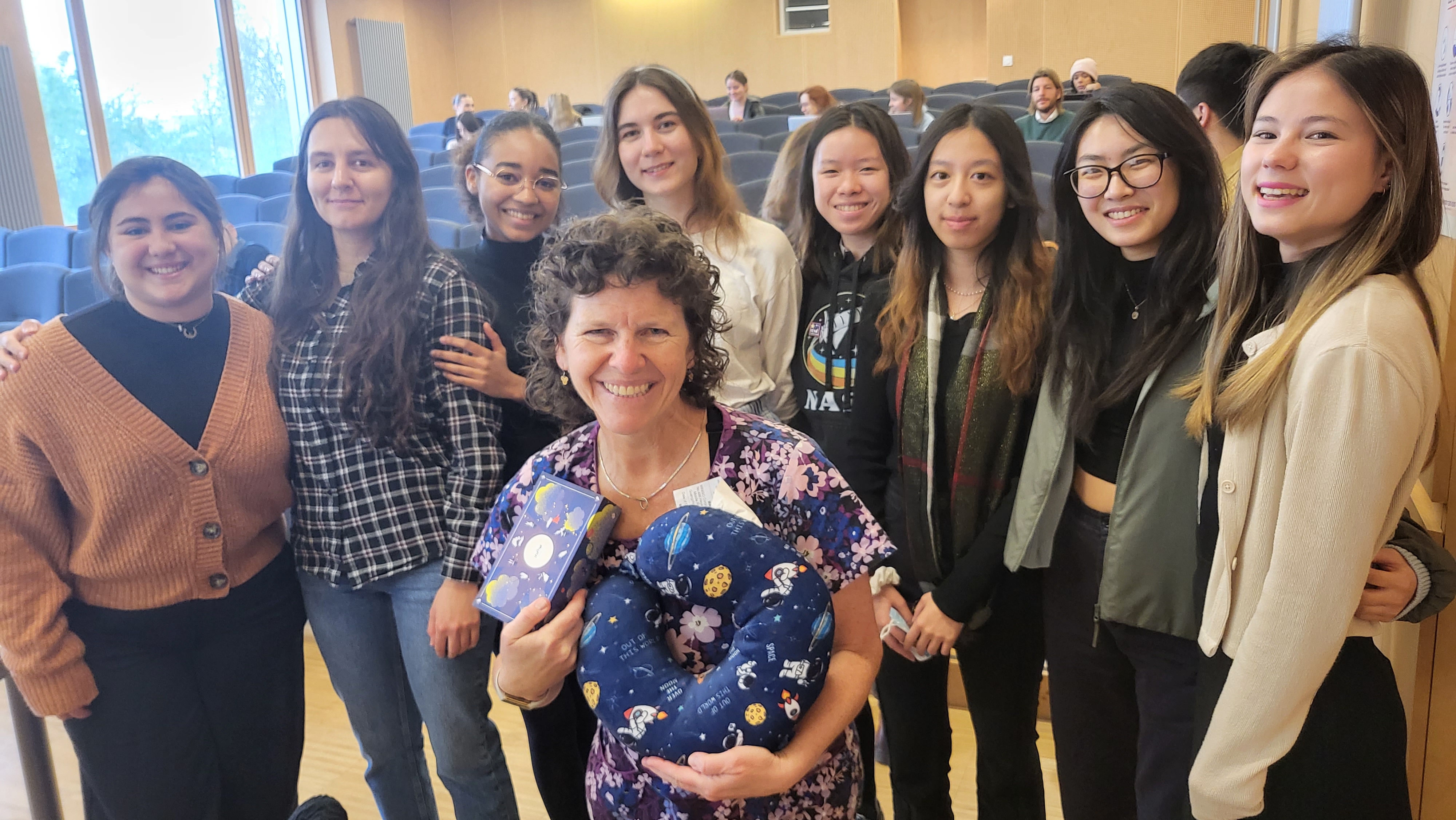 A group of females with their professor, another woman, crouching in front holding gifts.