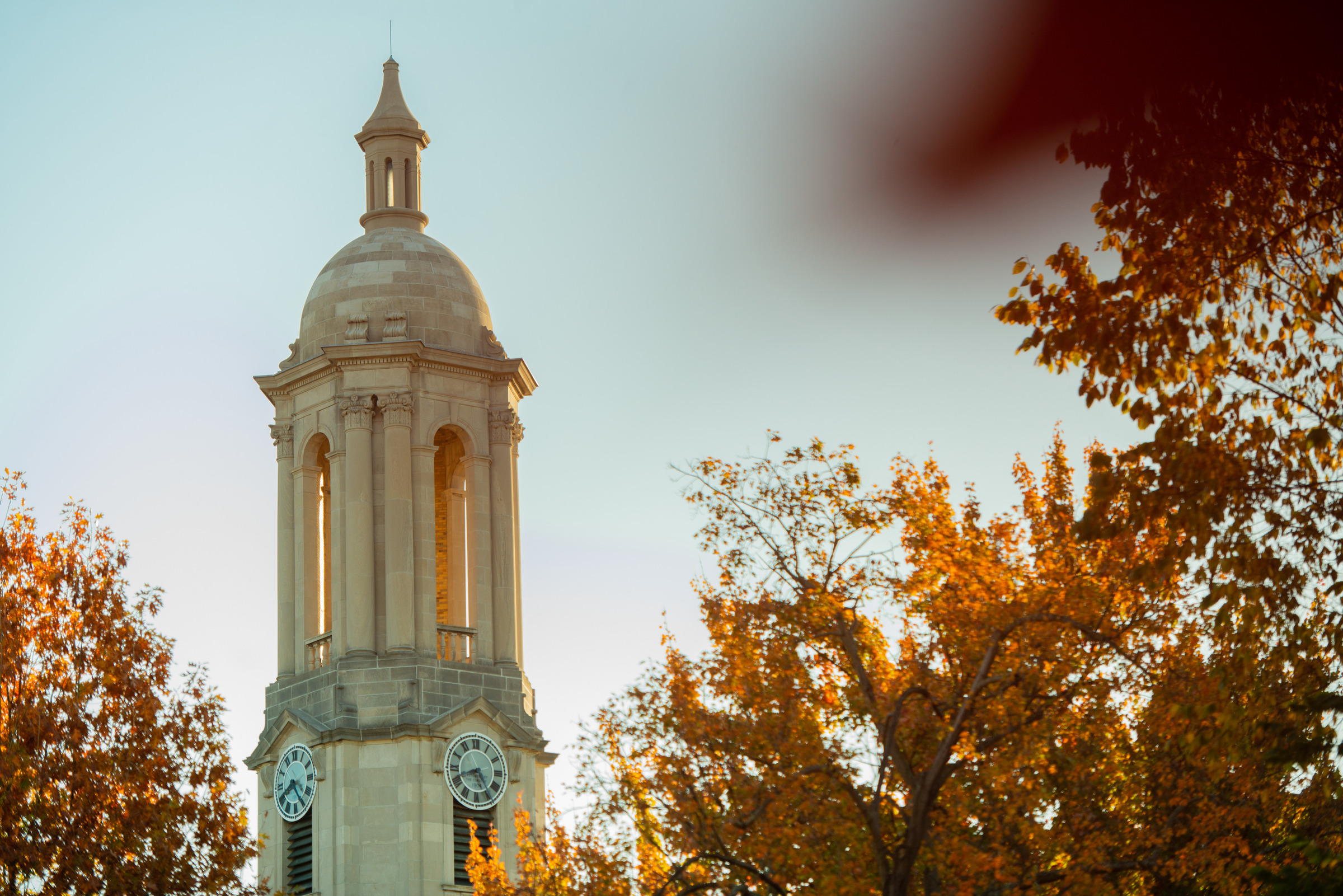 Old Main bell tower flanked by orange and yellow fall foliage