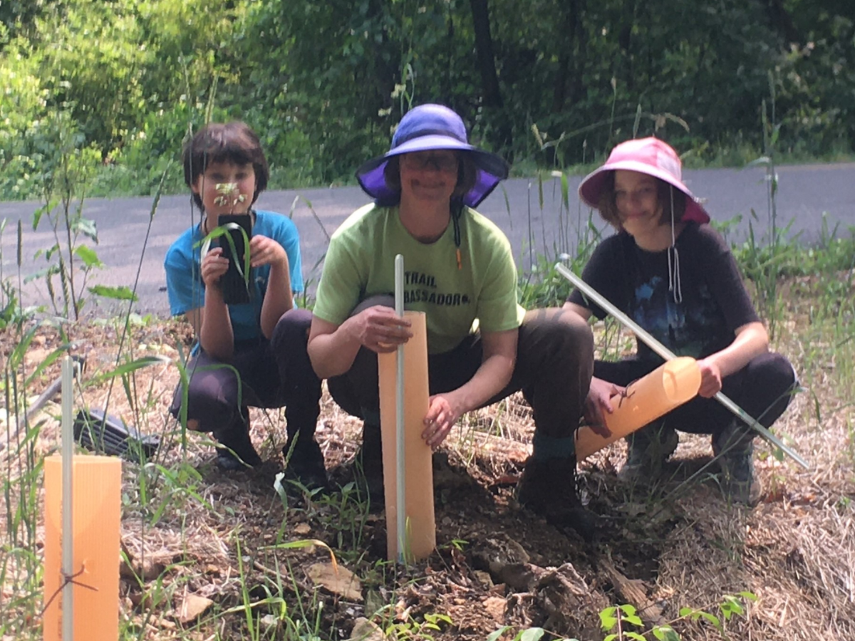 Jayne crouches on the ground with two kids as they do yard work