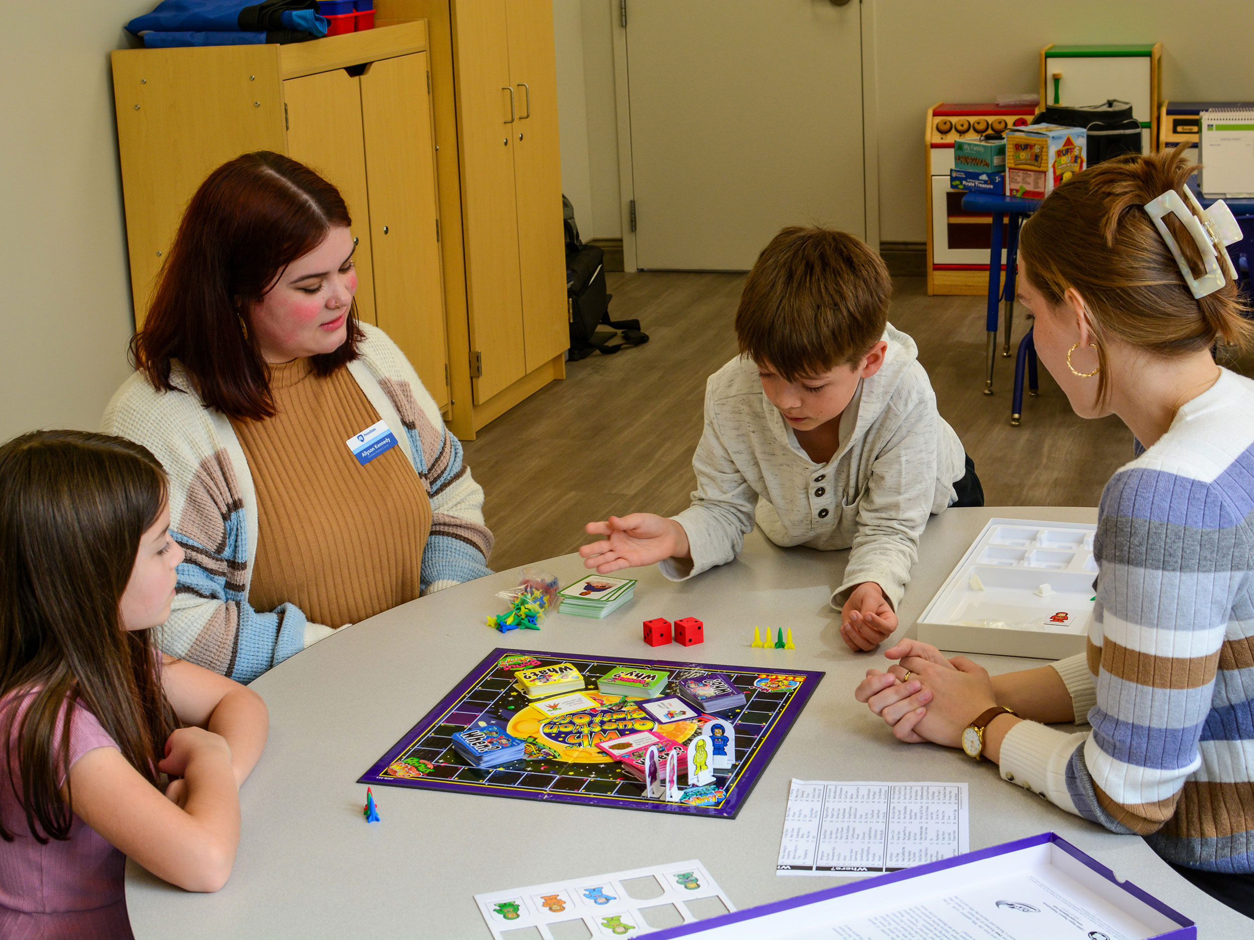 Two speech language pathology students play a therapeutic board game with 2 children