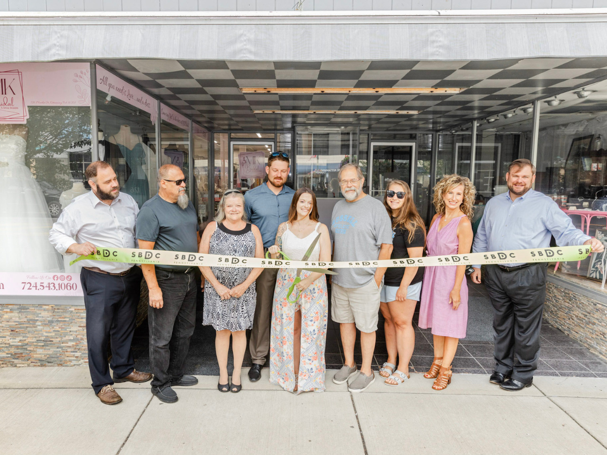 A group of people pose for a photograph, with the person in the center holding giant shears to cut a ribbon 