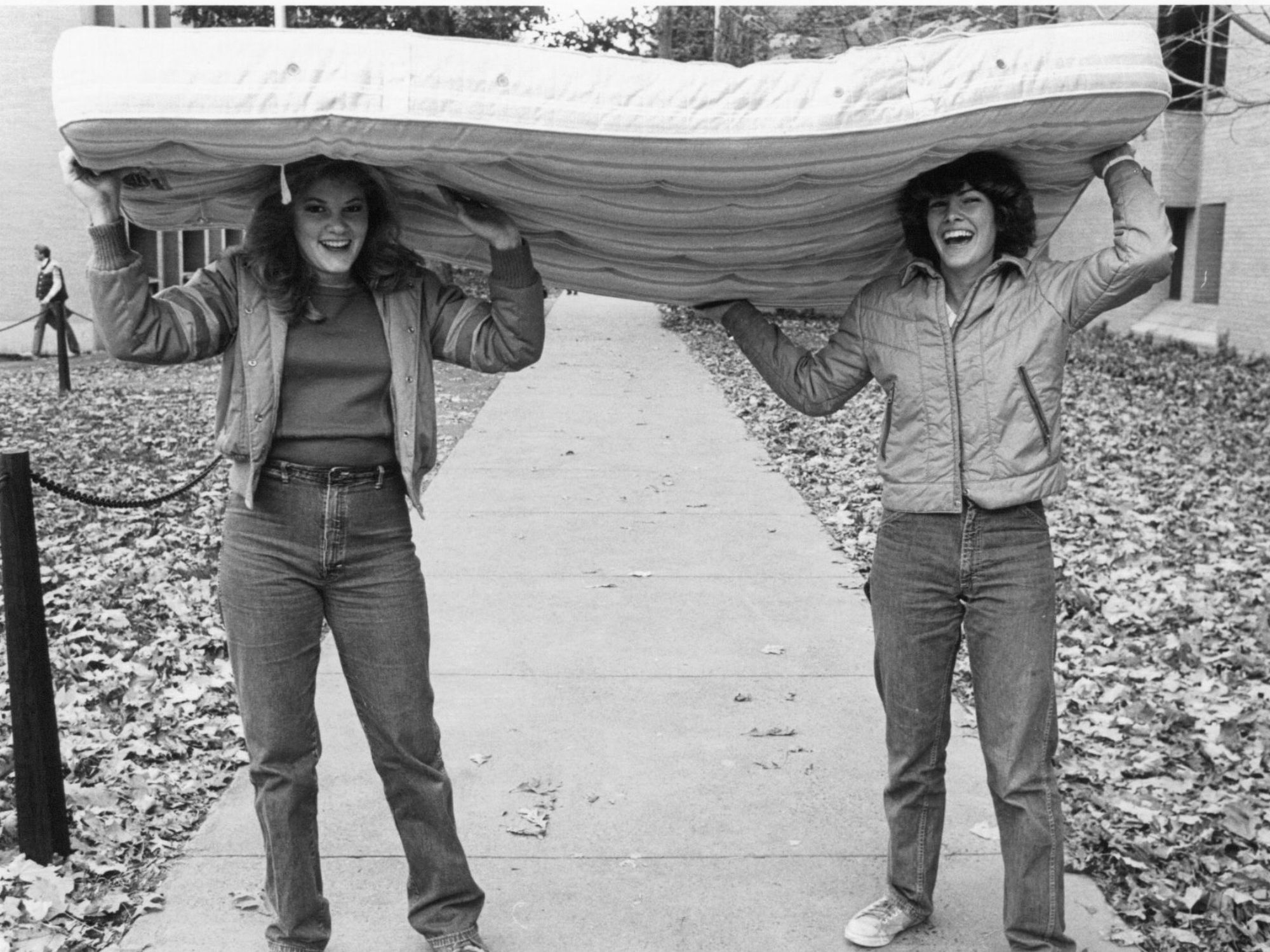 Two female students carry a mattress on their heads