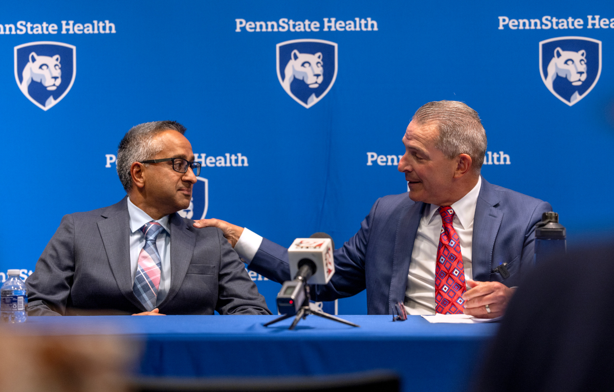 Two men in suits sit next to each other, talking and smiling.