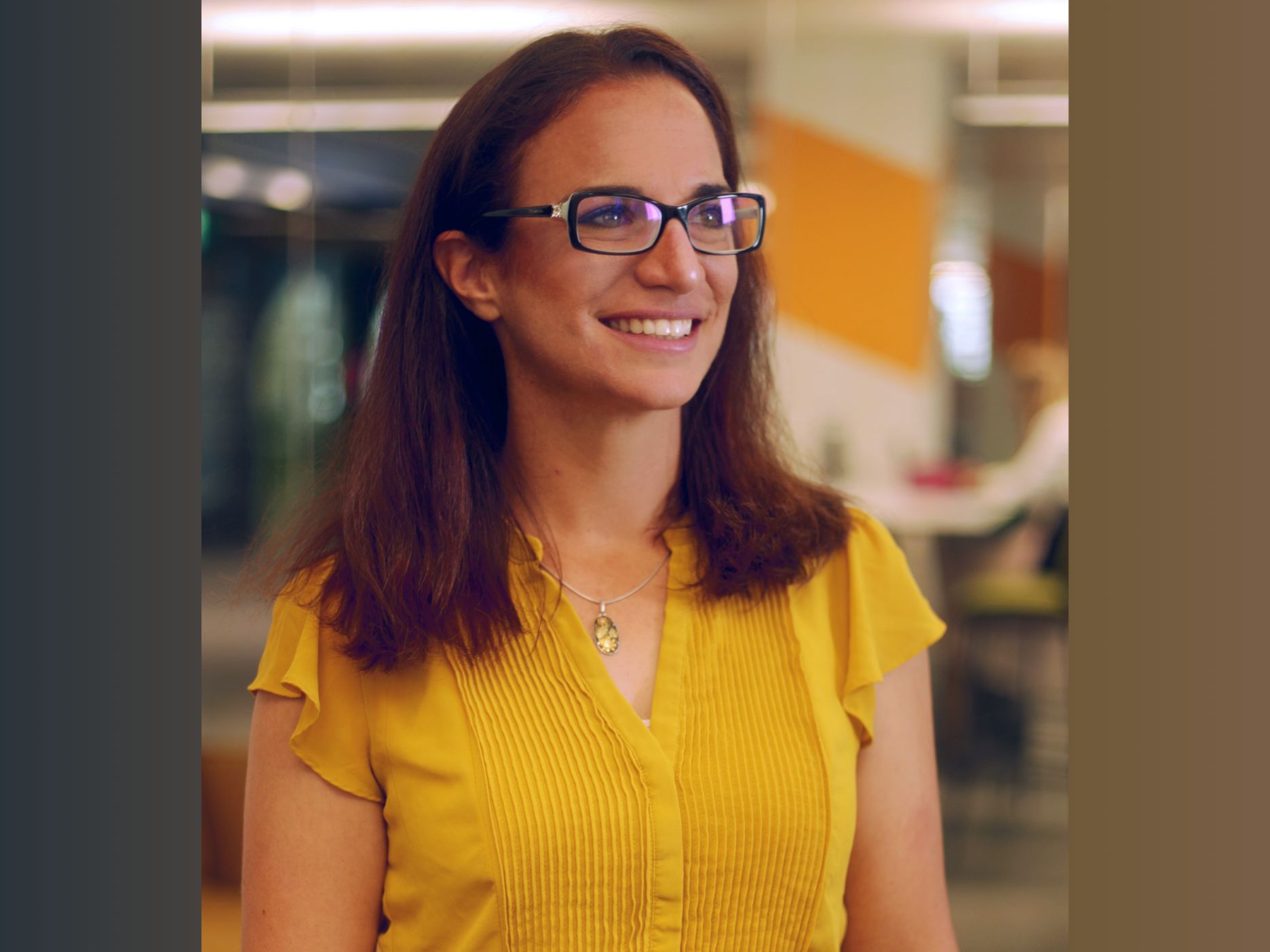 smiling person with long brown hair, glasses, yellow shirt