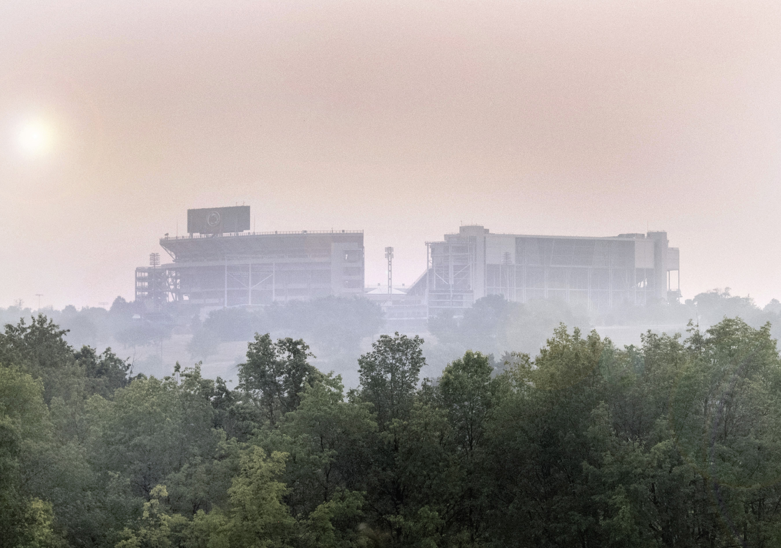 Beaver Stadium shrouded by smoke from Canadian wildfires, with trees in the foreground