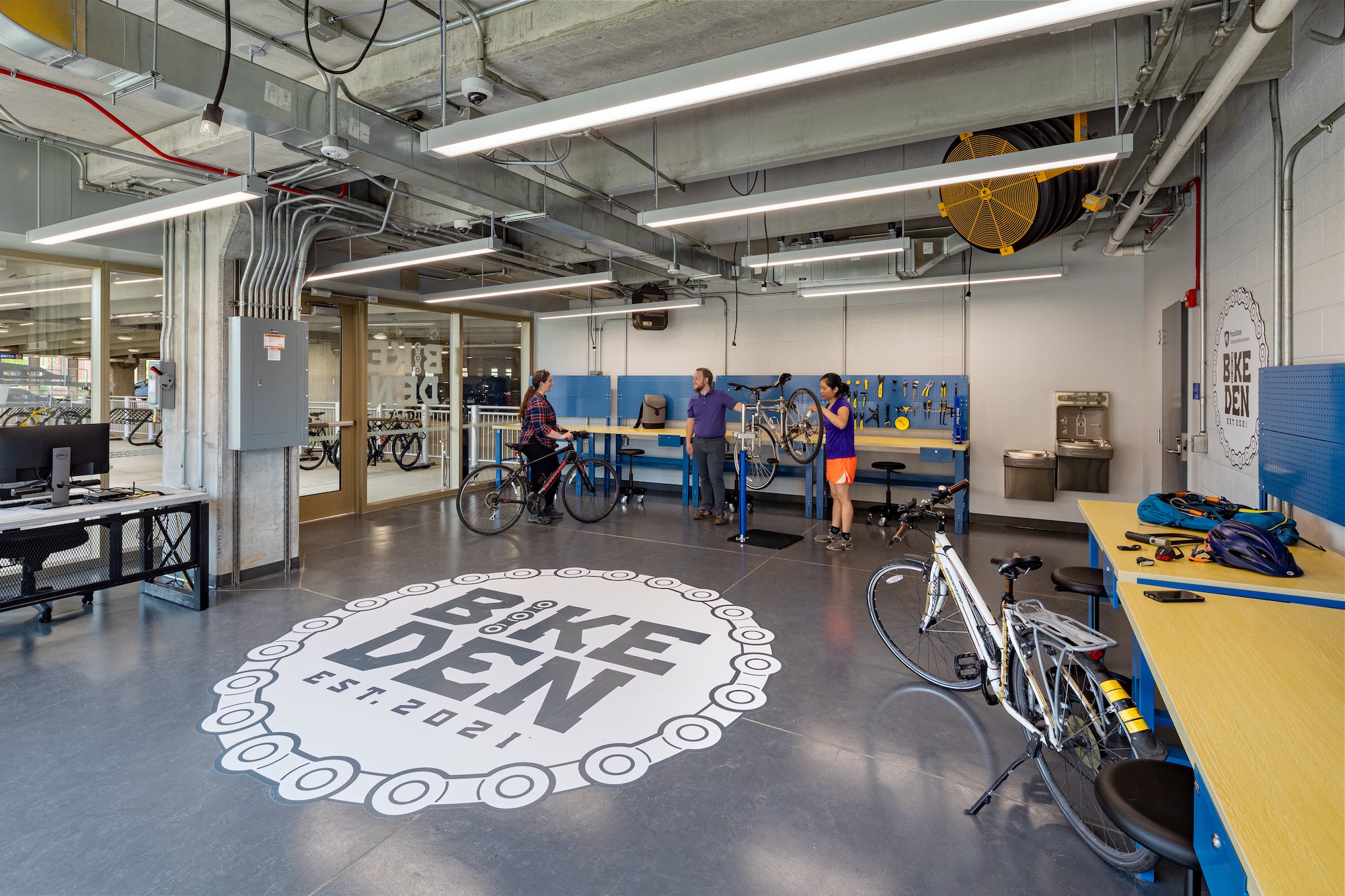 The interior of the Bike Den, showing a large Bike Den logo on the floor and people talking