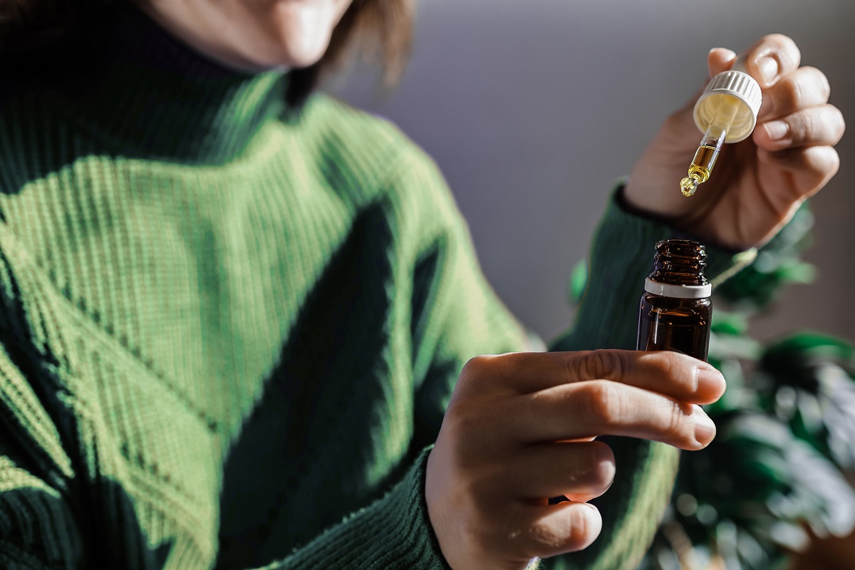 Woman holding a dropper of sublingual CBD cannabis hemp oil.