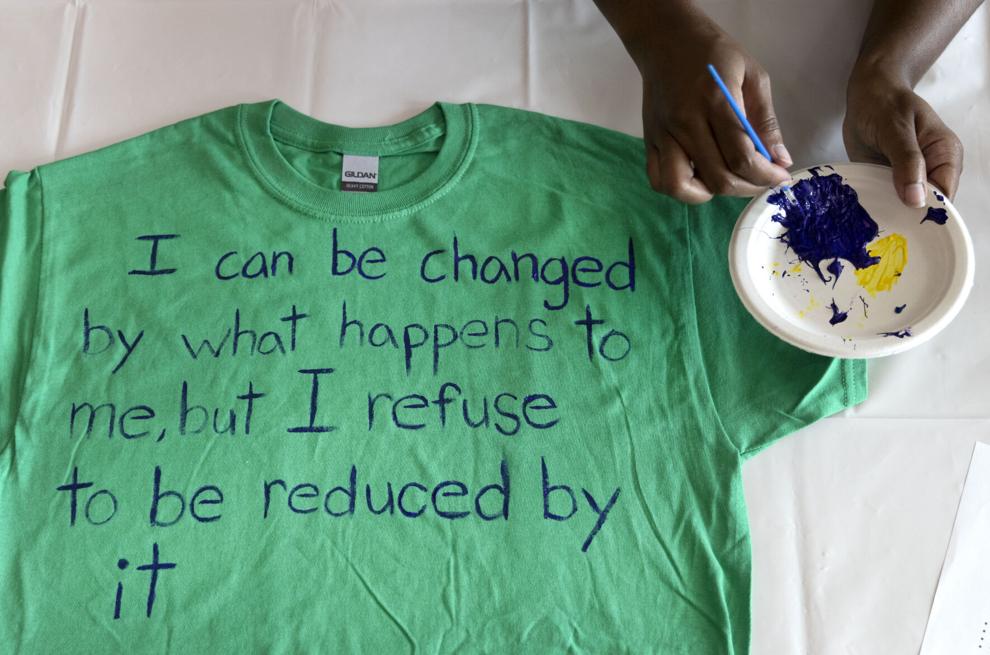 A green t-shirt with painted words reading I can be changed by what happens to me but I refuse to be reduced by it 