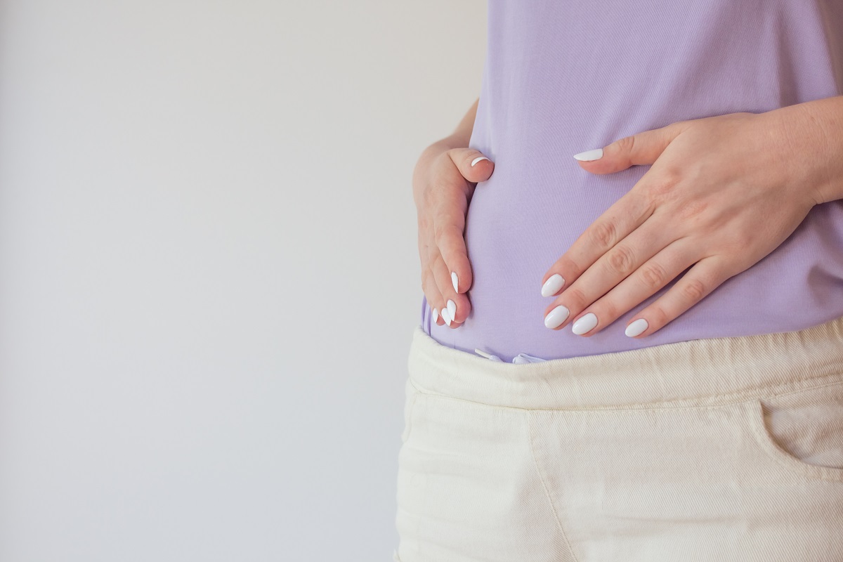 A pregnant person holds their hands over their abdomen. 