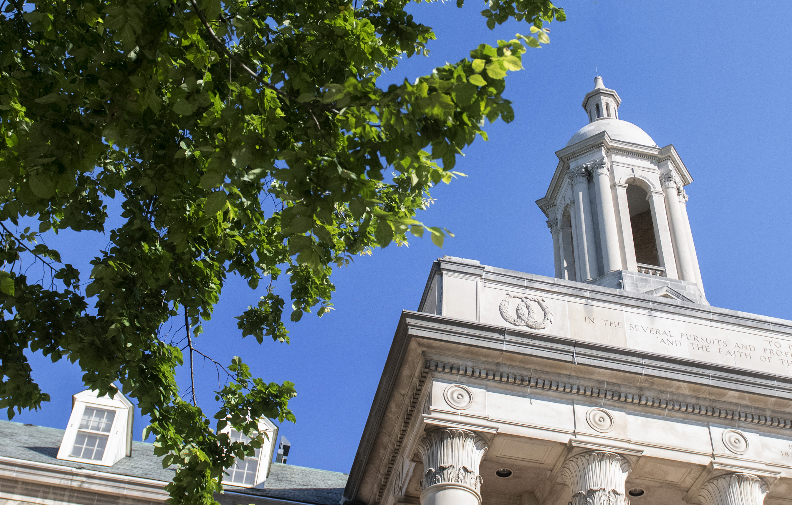 The tower of Old Main building above the trees against a brilliant blue sky