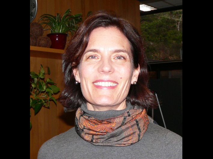 Headshot of smiling person wearing orange and plaid scarf