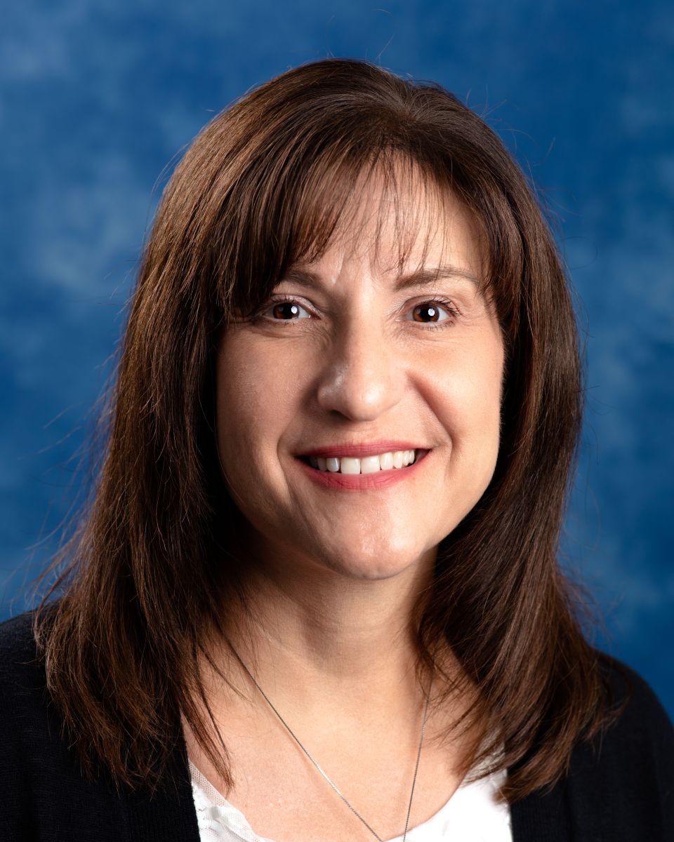 Woman with brown hair wearing a white shirt with black sweater over it.