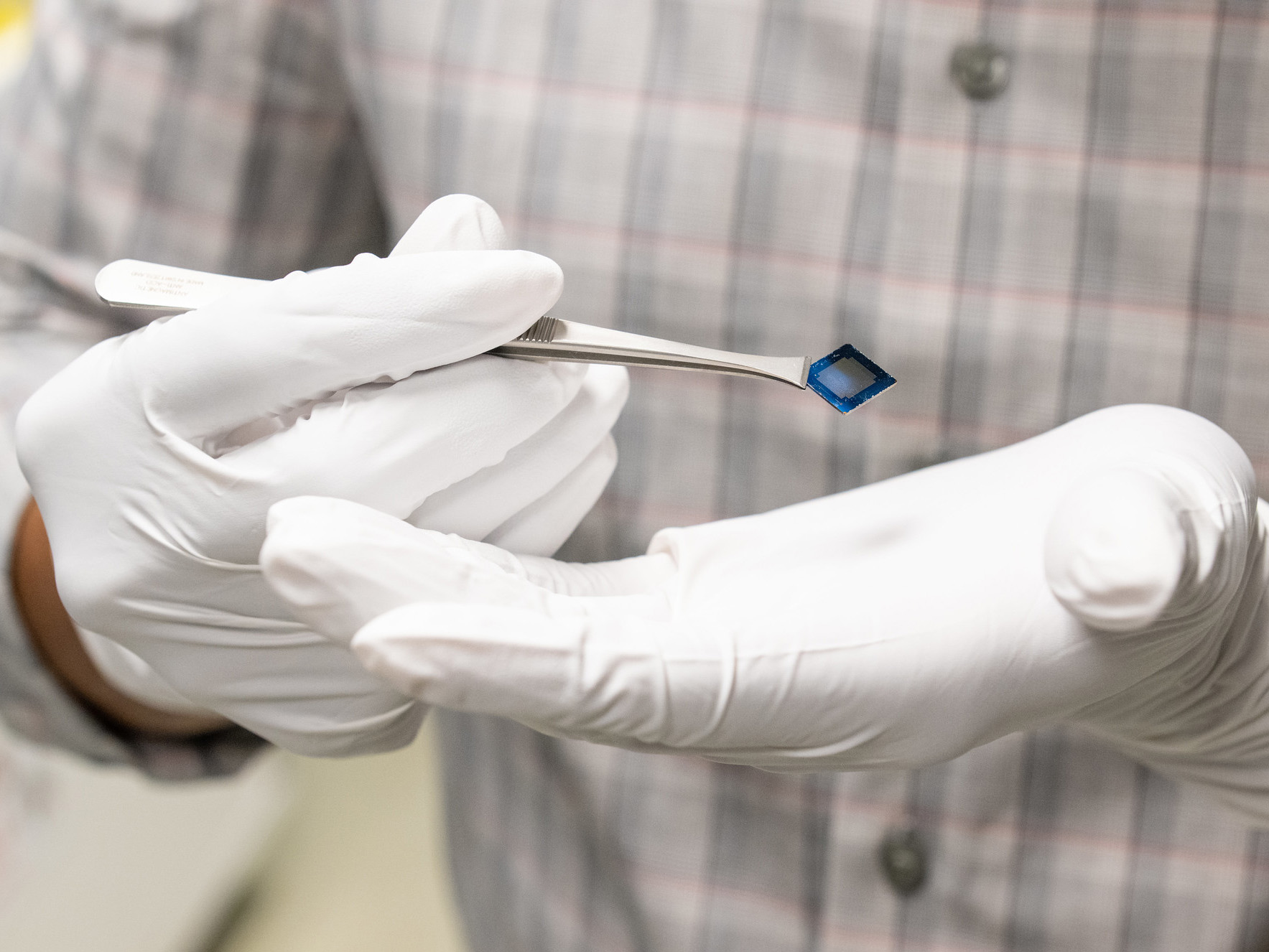 Gloved hands hold tweezers with a tiny computer chip