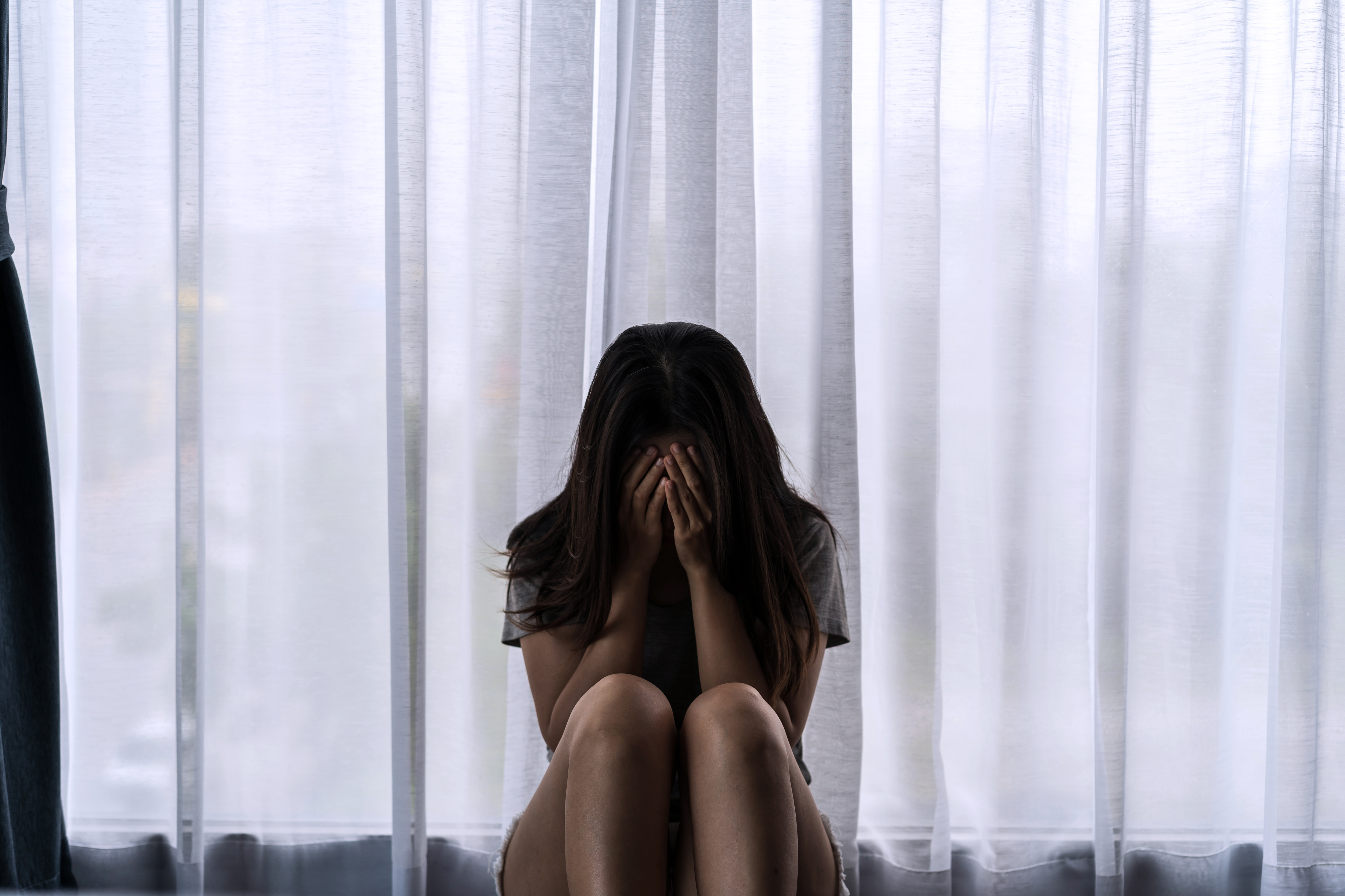 A woman sitting in front of a window with her face in her hands.