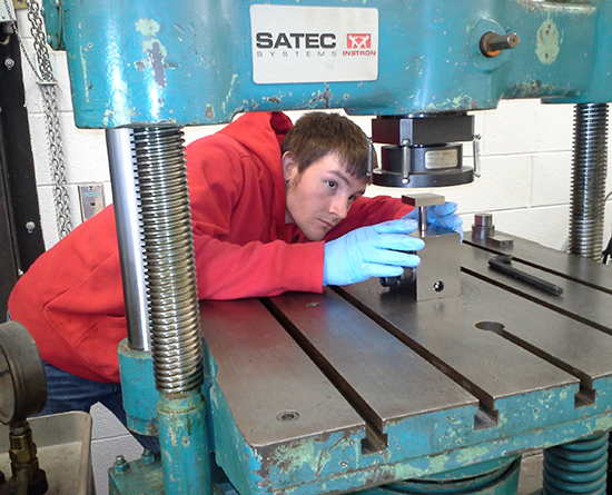 Person in a red hoodie and blue gloves works with a metal machine