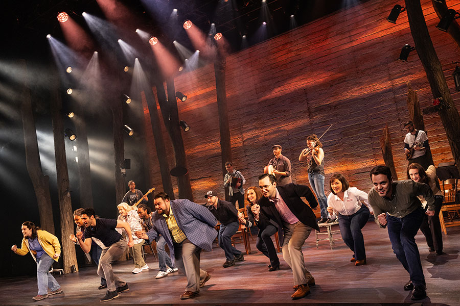 An all-ages diverse group of people dance and sing in unison on a stage.